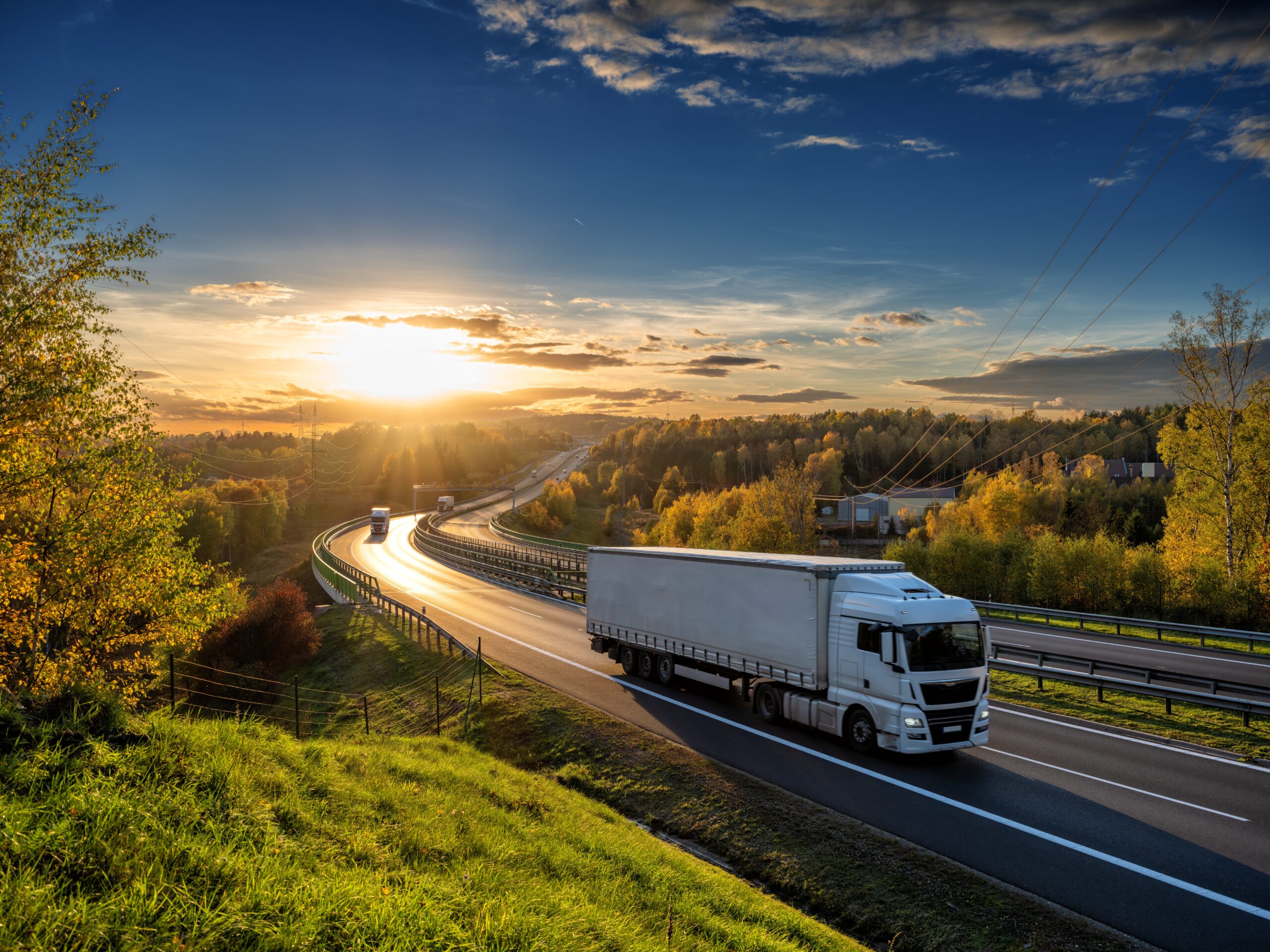 White,Trucks,Driving,On,The,Highway,Winding,Through,Forested,Landscape